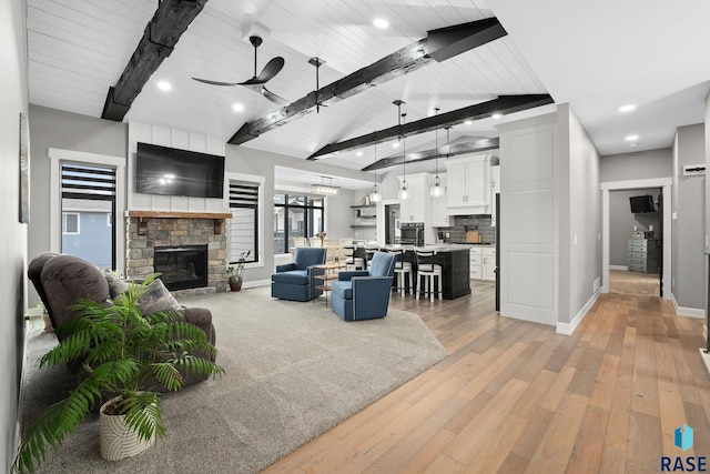 living area with a ceiling fan, vaulted ceiling with beams, a fireplace, and baseboards