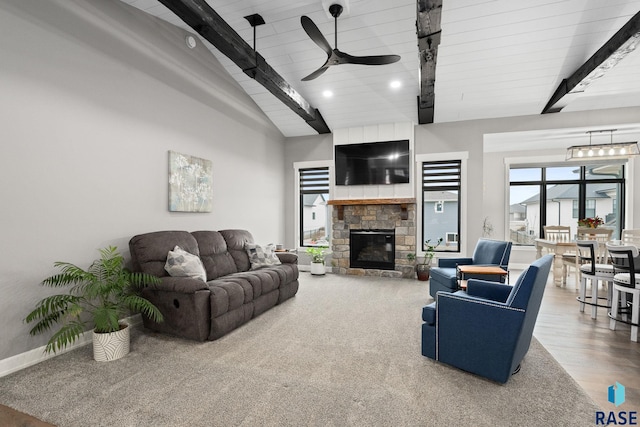 living area with vaulted ceiling with beams, ceiling fan, wood finished floors, and a stone fireplace