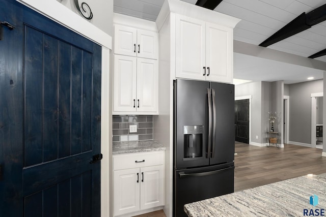 kitchen featuring light stone counters, wood finished floors, beam ceiling, black refrigerator with ice dispenser, and backsplash