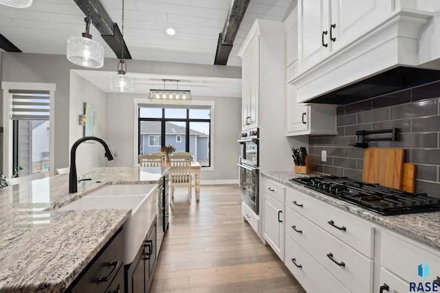 kitchen featuring tasteful backsplash, a sink, black gas cooktop, custom exhaust hood, and beam ceiling