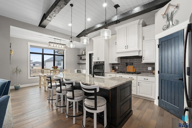 kitchen with tasteful backsplash, hardwood / wood-style flooring, light stone countertops, a kitchen island with sink, and gas cooktop