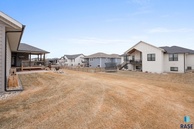 view of yard featuring a trampoline, a residential view, fence, and a wooden deck