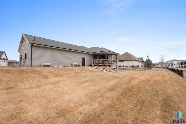 back of property with a yard, roof with shingles, and fence