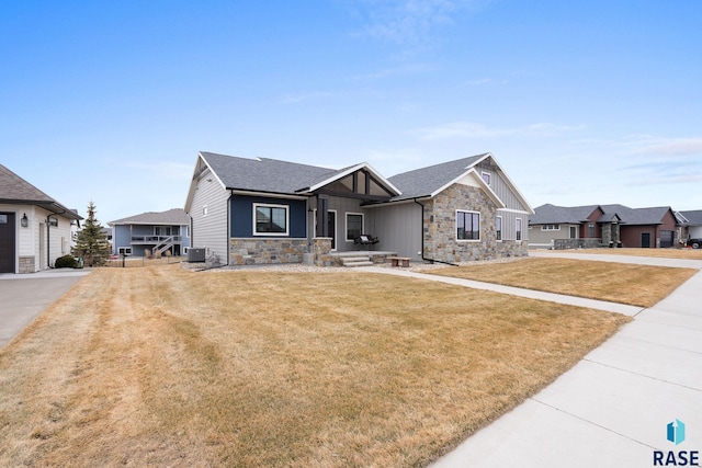 view of front of property with stone siding, central AC, a front yard, and roof with shingles