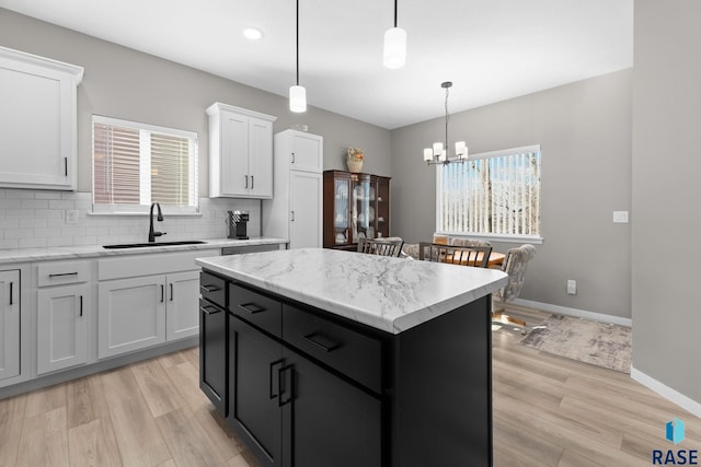 kitchen with a kitchen island, a sink, white cabinets, backsplash, and light wood finished floors