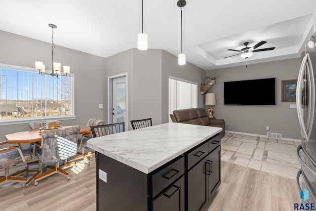 kitchen with a raised ceiling, light countertops, open floor plan, a kitchen island, and light wood-type flooring