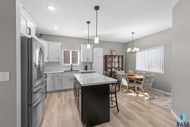 kitchen featuring a sink, light wood-type flooring, decorative backsplash, a center island, and stainless steel fridge