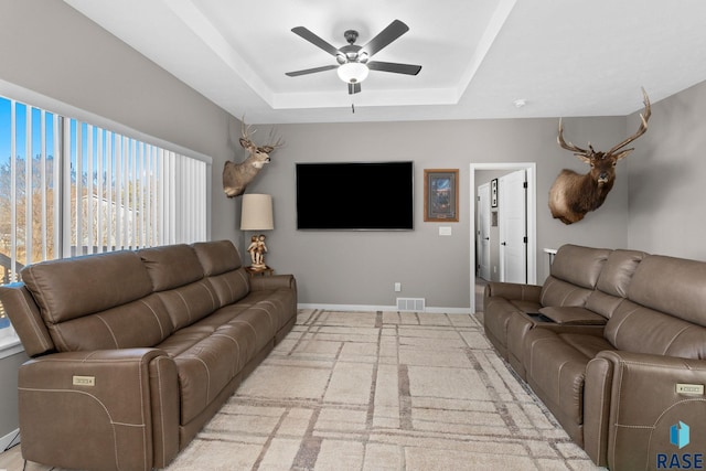 living area featuring a raised ceiling, visible vents, ceiling fan, and baseboards