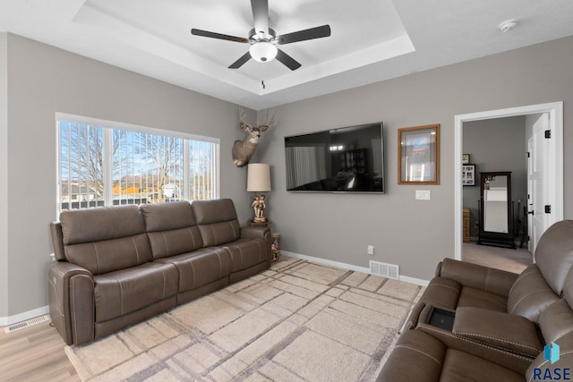 living area featuring ceiling fan, a raised ceiling, visible vents, and baseboards