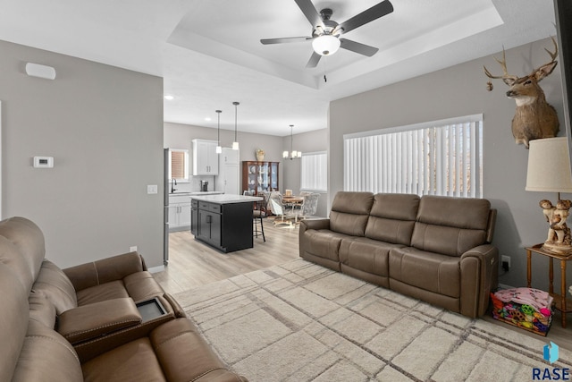 living room with light wood finished floors, a raised ceiling, and a healthy amount of sunlight