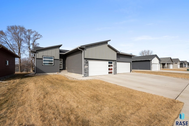 view of front of property with a garage, driveway, stone siding, a front lawn, and board and batten siding