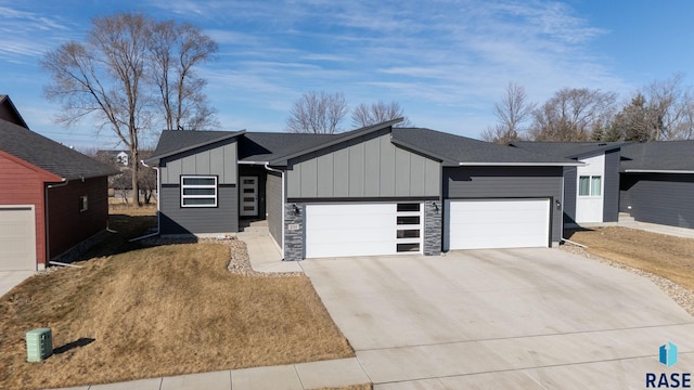 view of front of home featuring a shingled roof, an attached garage, board and batten siding, stone siding, and driveway