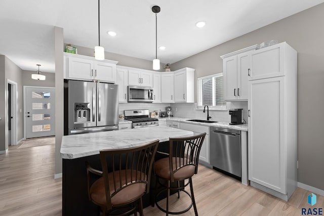 kitchen with backsplash, appliances with stainless steel finishes, white cabinets, a sink, and a kitchen island