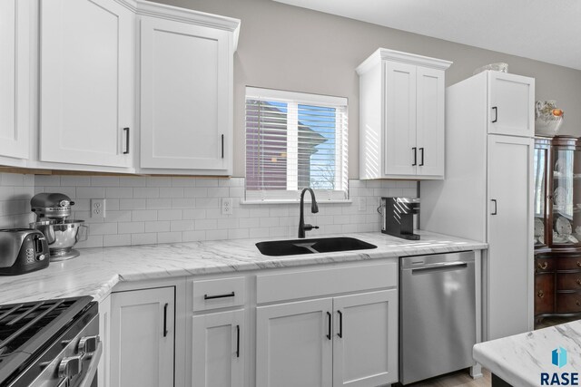 kitchen with light stone counters, stainless steel appliances, a sink, white cabinets, and decorative backsplash