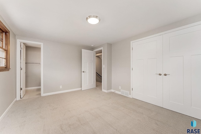 unfurnished bedroom featuring light colored carpet, a closet, visible vents, and baseboards