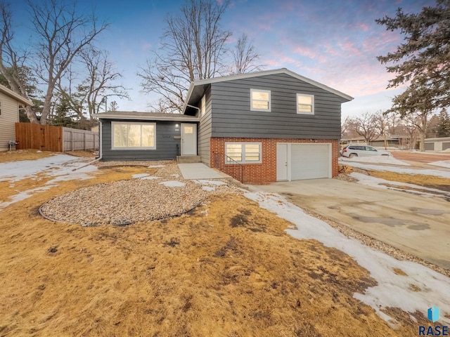 split level home featuring a garage, driveway, brick siding, and fence