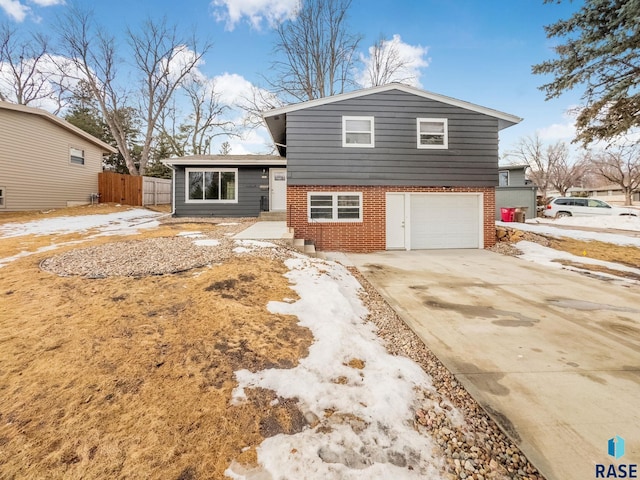 tri-level home with a garage, concrete driveway, brick siding, and fence