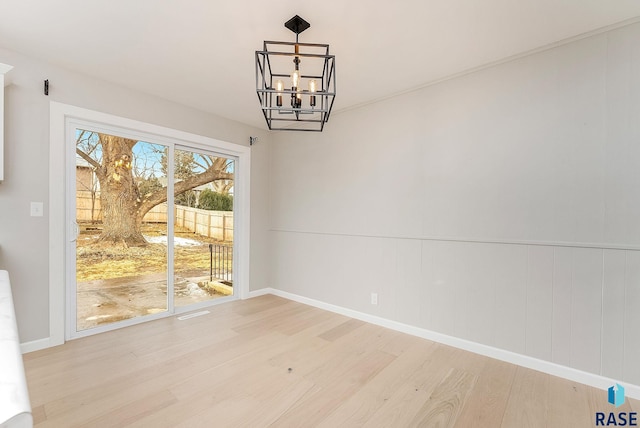 unfurnished dining area with a chandelier, baseboards, and wood finished floors