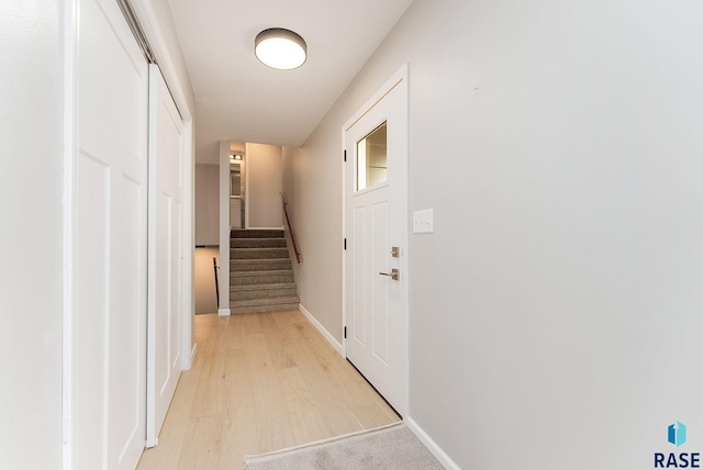 hall featuring light wood finished floors, stairs, and baseboards