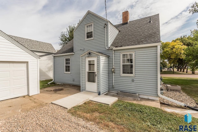 back of house featuring a garage, a shingled roof, and a chimney