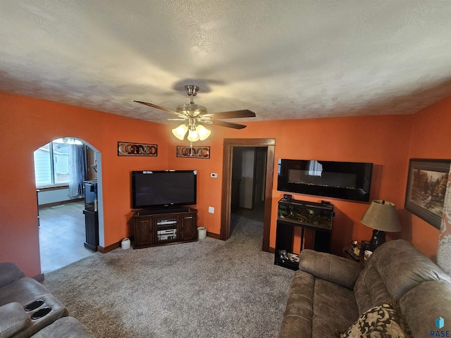 living room featuring arched walkways, a textured ceiling, carpet floors, a ceiling fan, and baseboards