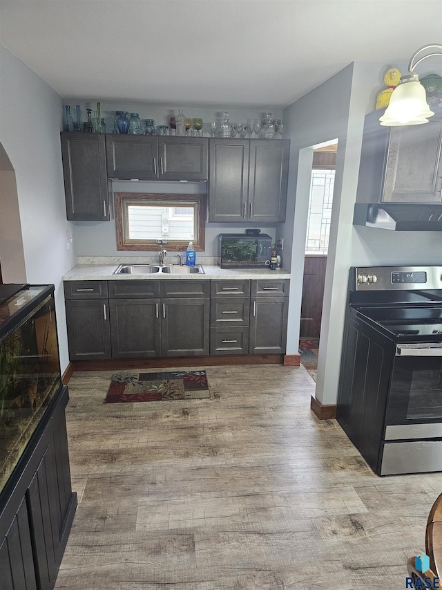 kitchen with stainless steel electric stove, a wealth of natural light, light countertops, light wood-style floors, and a sink