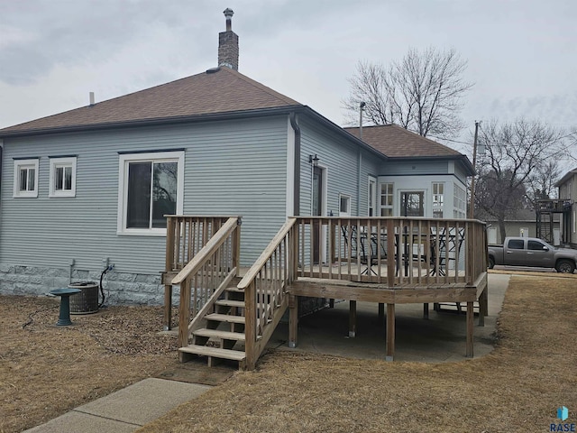 rear view of house featuring a deck, a shingled roof, a chimney, and central air condition unit