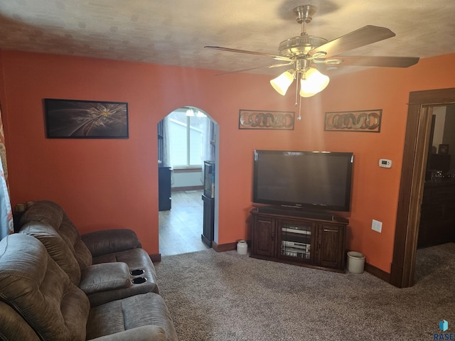 carpeted living area with arched walkways, a ceiling fan, and baseboards