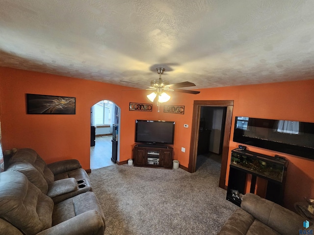 carpeted living room featuring baseboards, arched walkways, ceiling fan, and a textured ceiling