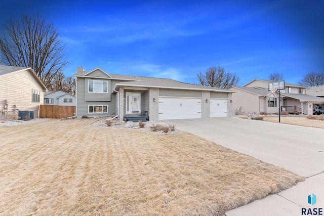 tri-level home with driveway, a chimney, an attached garage, fence, and brick siding