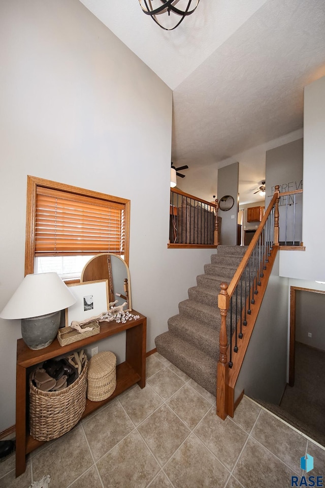 stairway with ceiling fan, baseboards, and tile patterned flooring