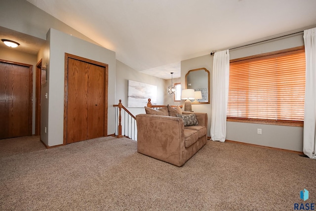 carpeted living area with a chandelier, vaulted ceiling, and baseboards