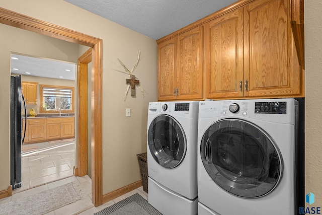 laundry area with cabinet space, light tile patterned floors, independent washer and dryer, a textured ceiling, and a sink