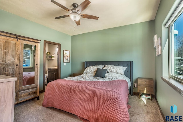 bedroom featuring a barn door, baseboards, connected bathroom, ceiling fan, and carpet floors