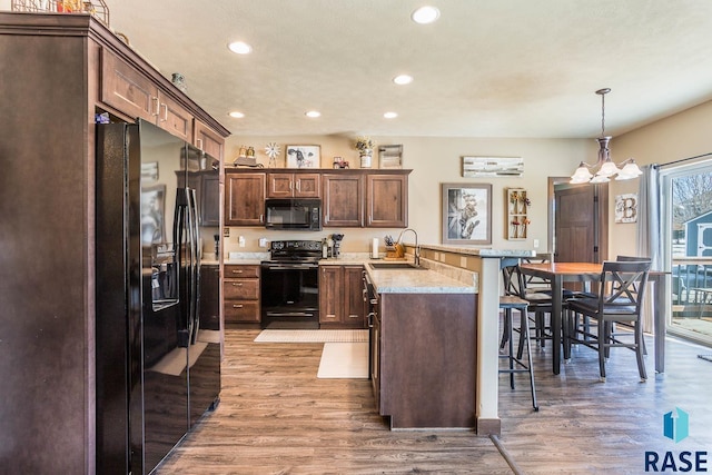 kitchen with a breakfast bar area, a peninsula, a sink, black appliances, and light wood finished floors