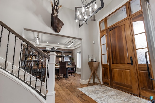 entrance foyer featuring a notable chandelier, a raised ceiling, stairway, wood finished floors, and baseboards