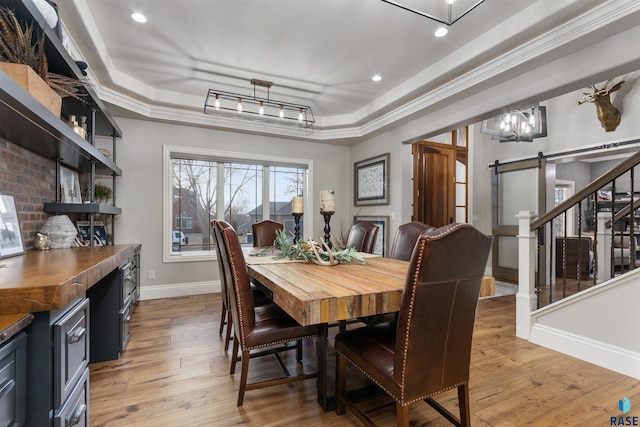 dining area with a barn door, a tray ceiling, light wood-style flooring, and baseboards