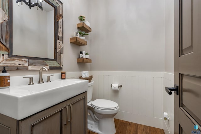 half bath with a wainscoted wall, vanity, toilet, and wood finished floors