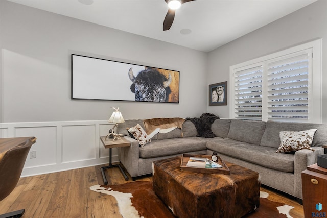 living area featuring a wainscoted wall, wood finished floors, a ceiling fan, and a decorative wall