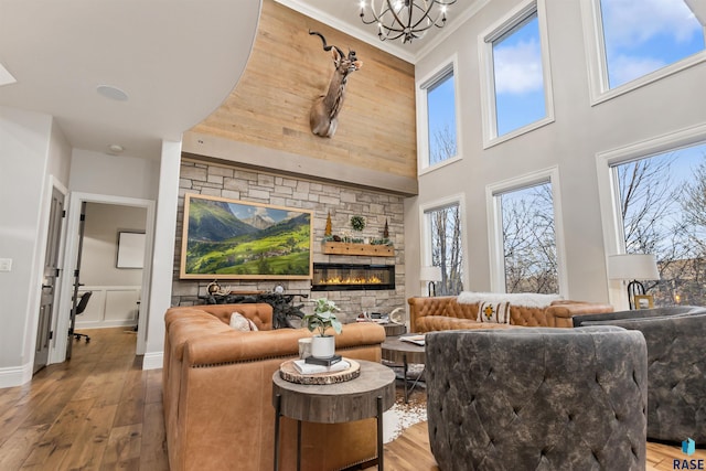 living room featuring a chandelier, a towering ceiling, ornamental molding, wood-type flooring, and a glass covered fireplace