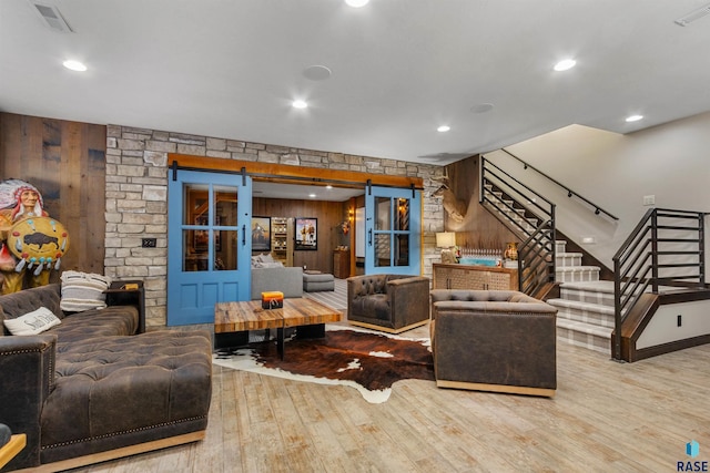 living room featuring wood finished floors, visible vents, stairway, and a barn door