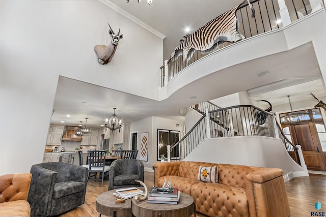 living room with a towering ceiling, wood finished floors, stairs, crown molding, and a notable chandelier