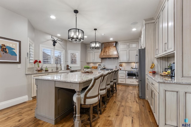 kitchen featuring premium range hood, a kitchen island, light wood-style flooring, and decorative backsplash