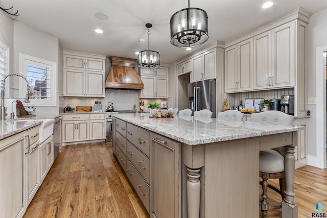 kitchen with high end appliances, a kitchen island, a breakfast bar area, custom exhaust hood, and light wood-type flooring