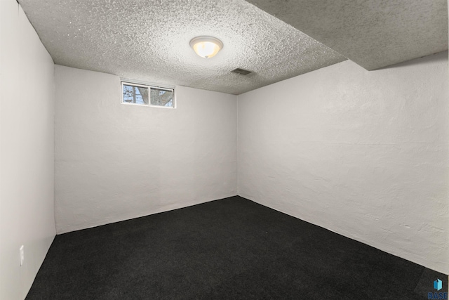 basement featuring carpet floors, visible vents, a textured wall, and a textured ceiling