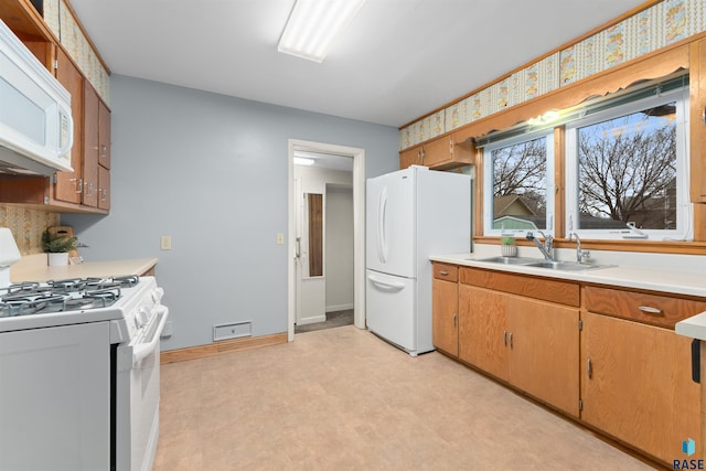 kitchen featuring light floors, light countertops, a sink, white appliances, and baseboards