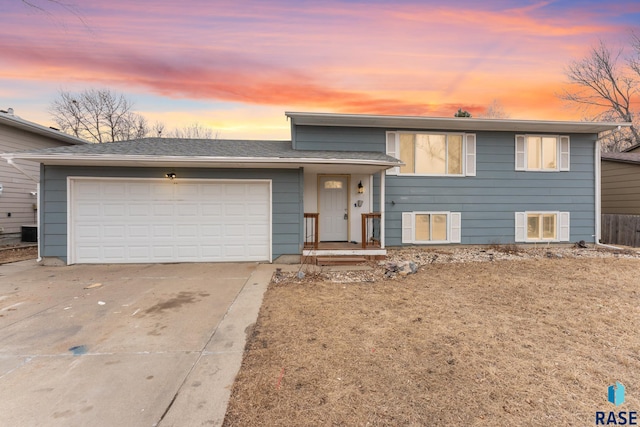 tri-level home featuring a garage, concrete driveway, and roof with shingles