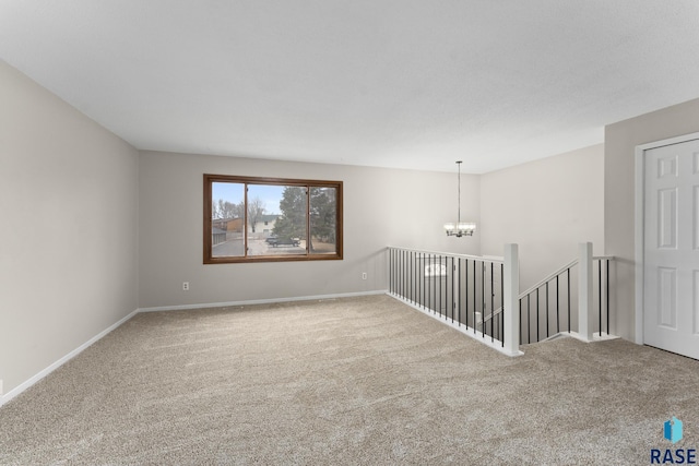 empty room featuring carpet floors, an inviting chandelier, and baseboards