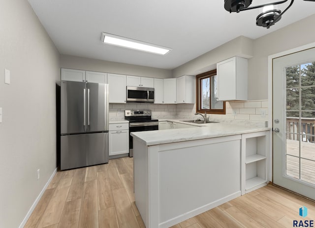 kitchen with tasteful backsplash, white cabinets, stainless steel appliances, light wood-type flooring, and a sink