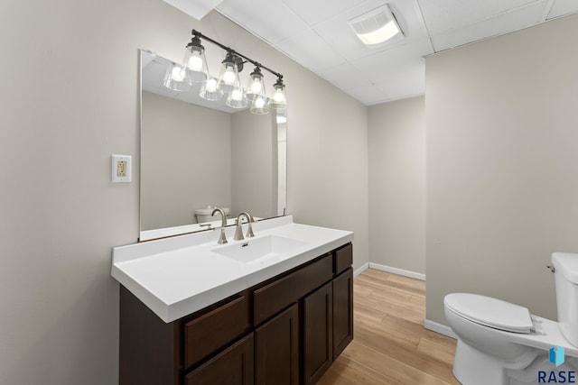 half bathroom with visible vents, toilet, wood finished floors, a drop ceiling, and baseboards